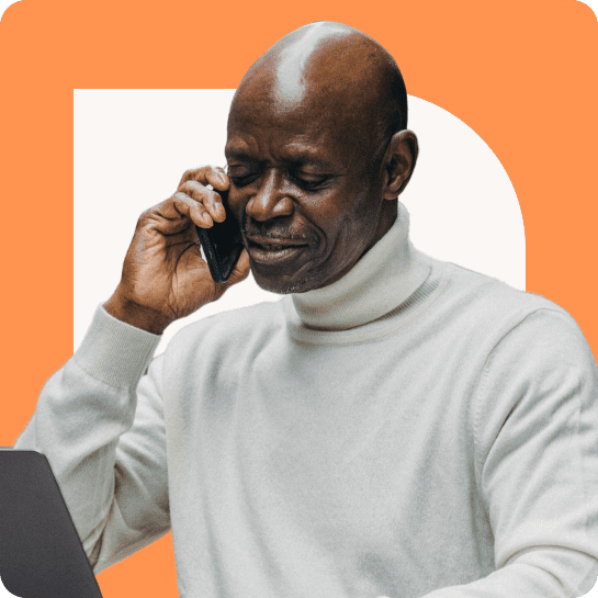 An older black man in a white sweater talks on a smartphone, with a laptop open in front of him, against an orange background.
